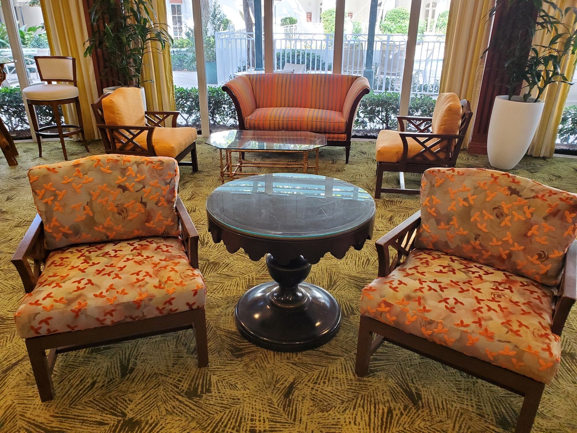 A seating area with patterned chairs, a striped sofa, and a glass top table in a lobby with large windows.