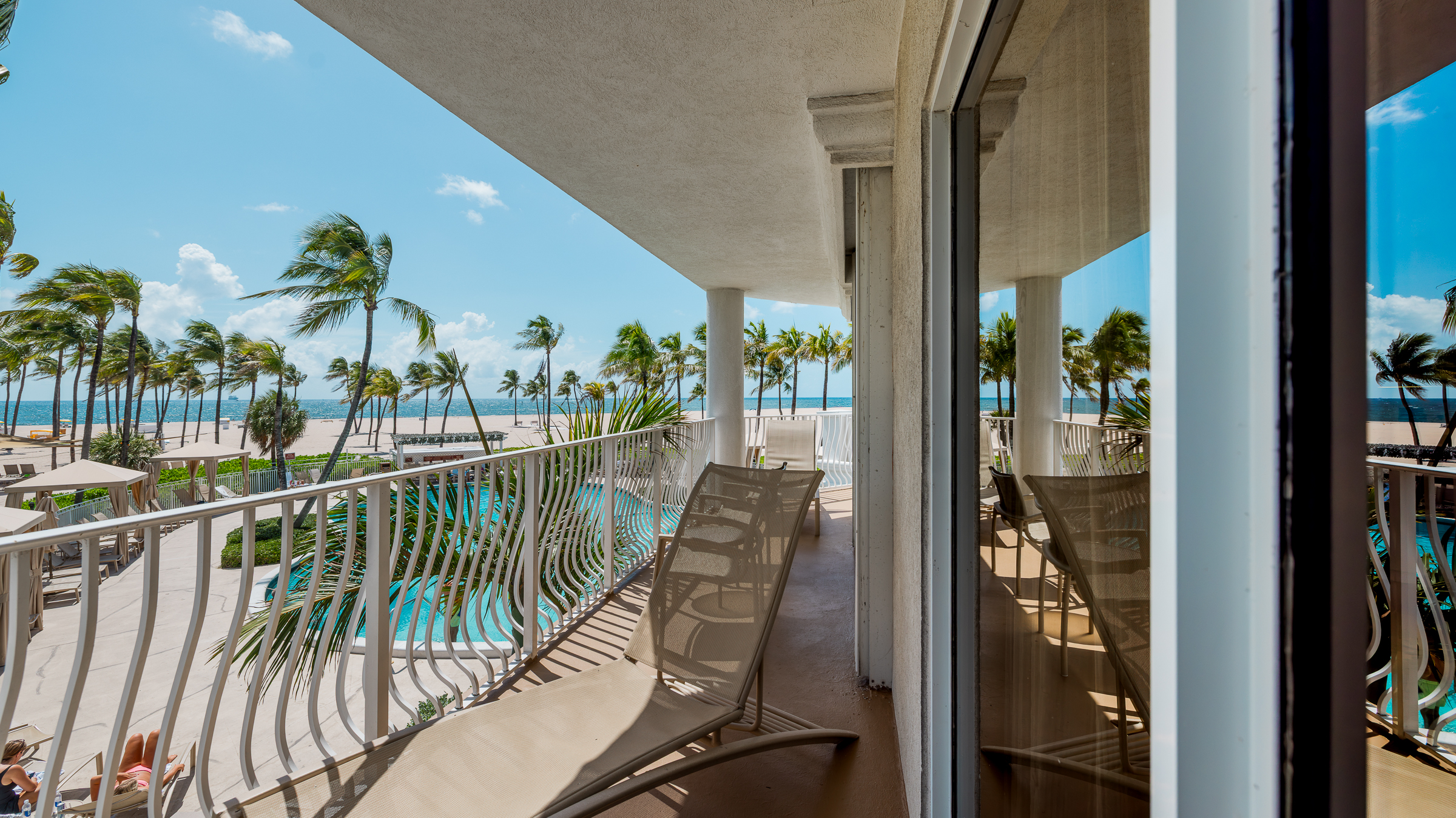A balcony with a view of the pool and beach